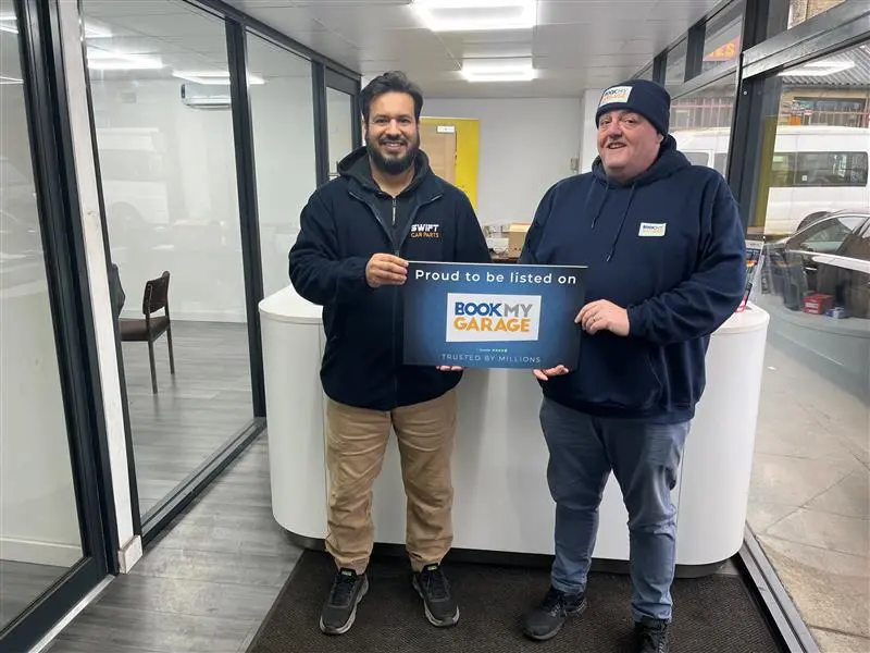 BookMyGarage employee stood next to owner of Merlin Motors Huddersfield holding BookMyGarage branded card